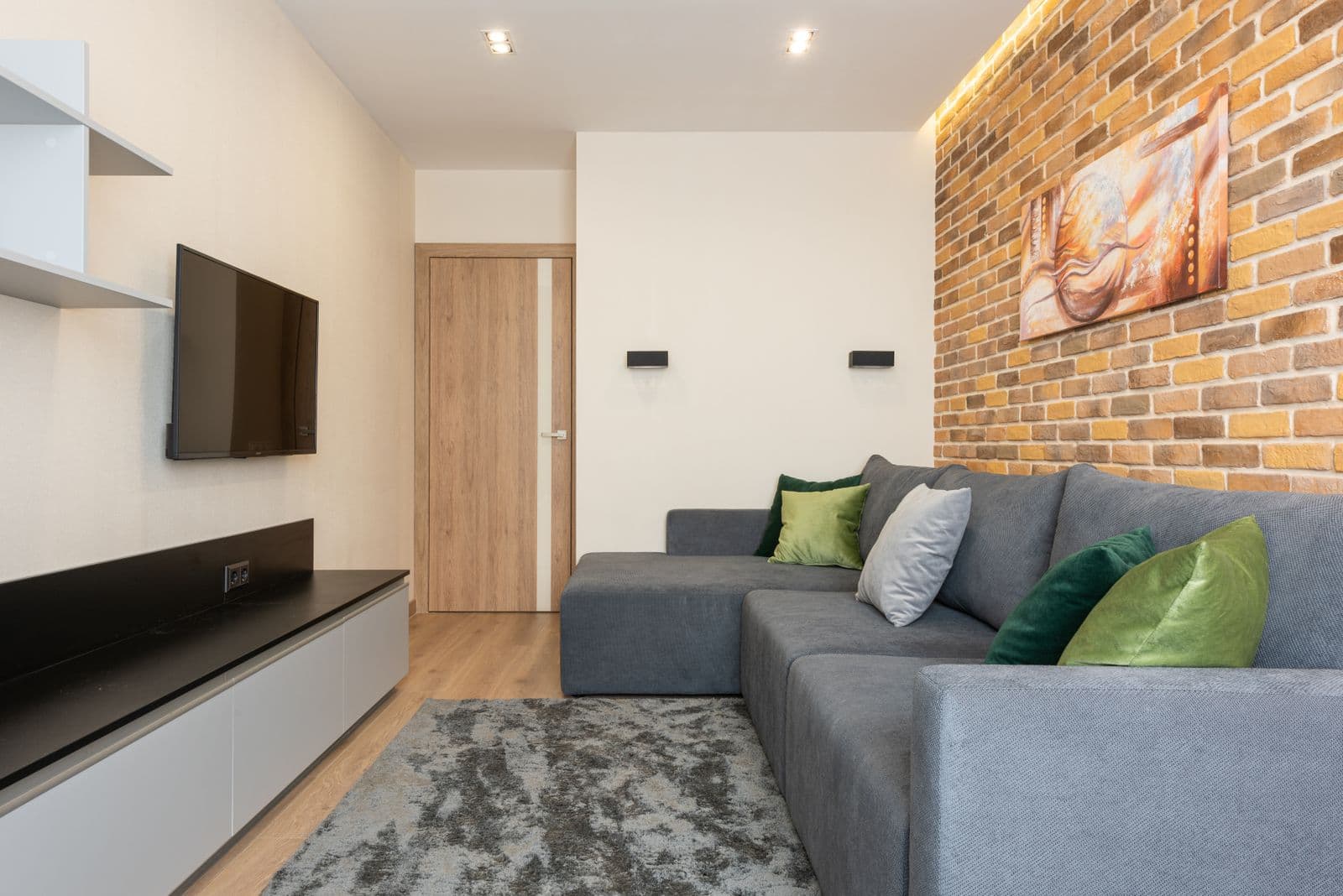 Living room with a TV mounted on a plain wall and an exposed brick accent wall behind the sofa